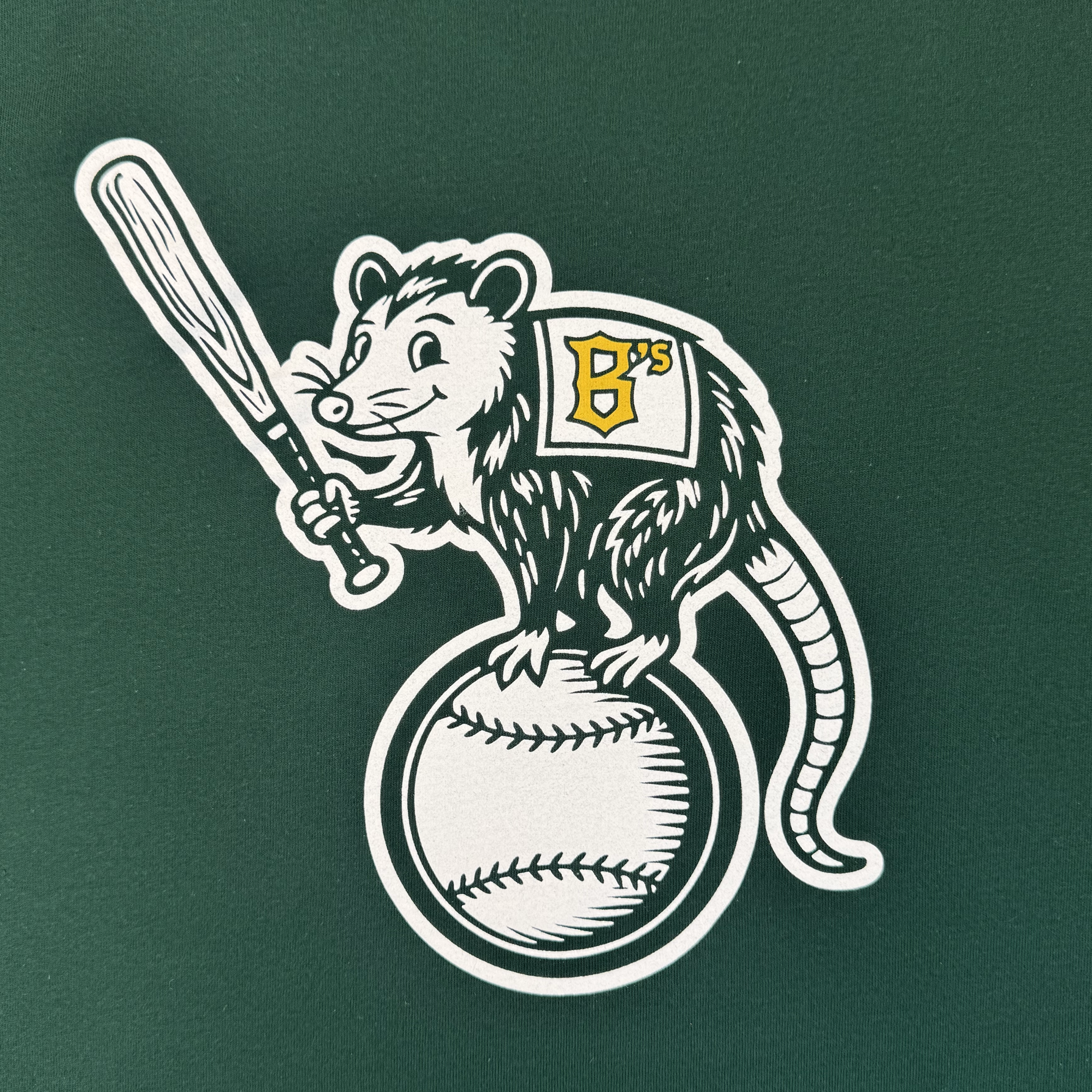 Cartoon opossum with a baseball bat stands on a baseball, wearing an Oakland Ballers jersey with a green "B's," set on solid green—featured on the Women's Clutch Tee by Oakland Ballers for the new Pioneer League team.