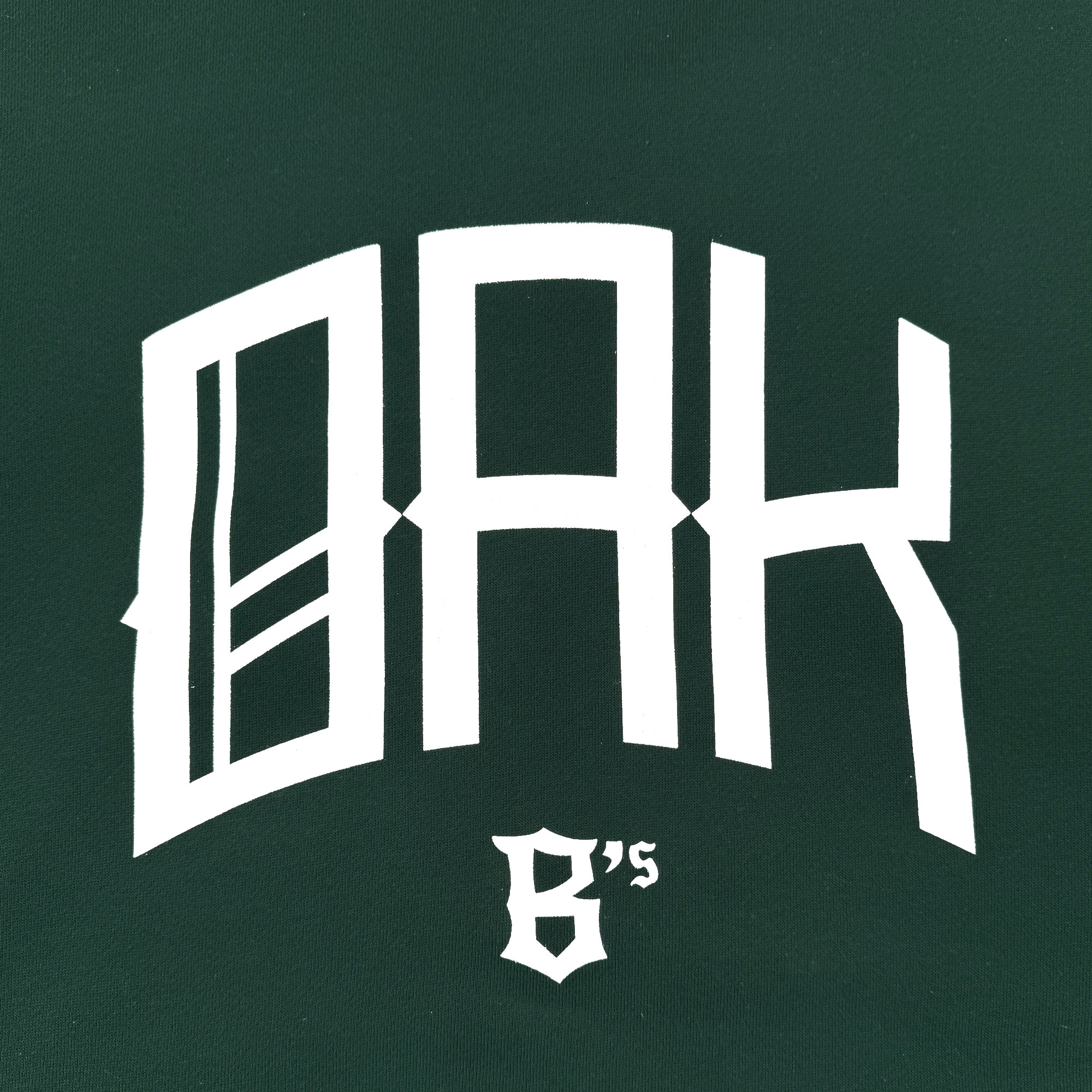 The OAK Ballers Hoodie by Oakland Ballers features bold white “OAK” text and ornate “6’s” on a dark green background, creating a modern, sporty design inspired by the team’s baseball heritage.