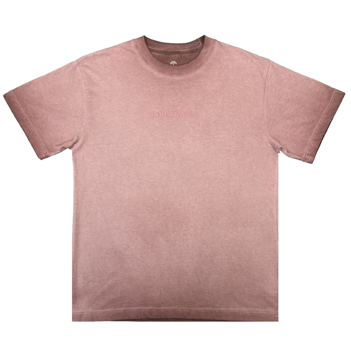 The Oaklandish Classic Logo Tee by Oaklandish is showcased laid flat on a white background. This short-sleeved men’s T-shirt, crafted from heavyweight cotton, features a crew neckline and subtle embossed “OAKLANDISH” text across the chest. The mauve fabric offers a lightly faded, vintage look.