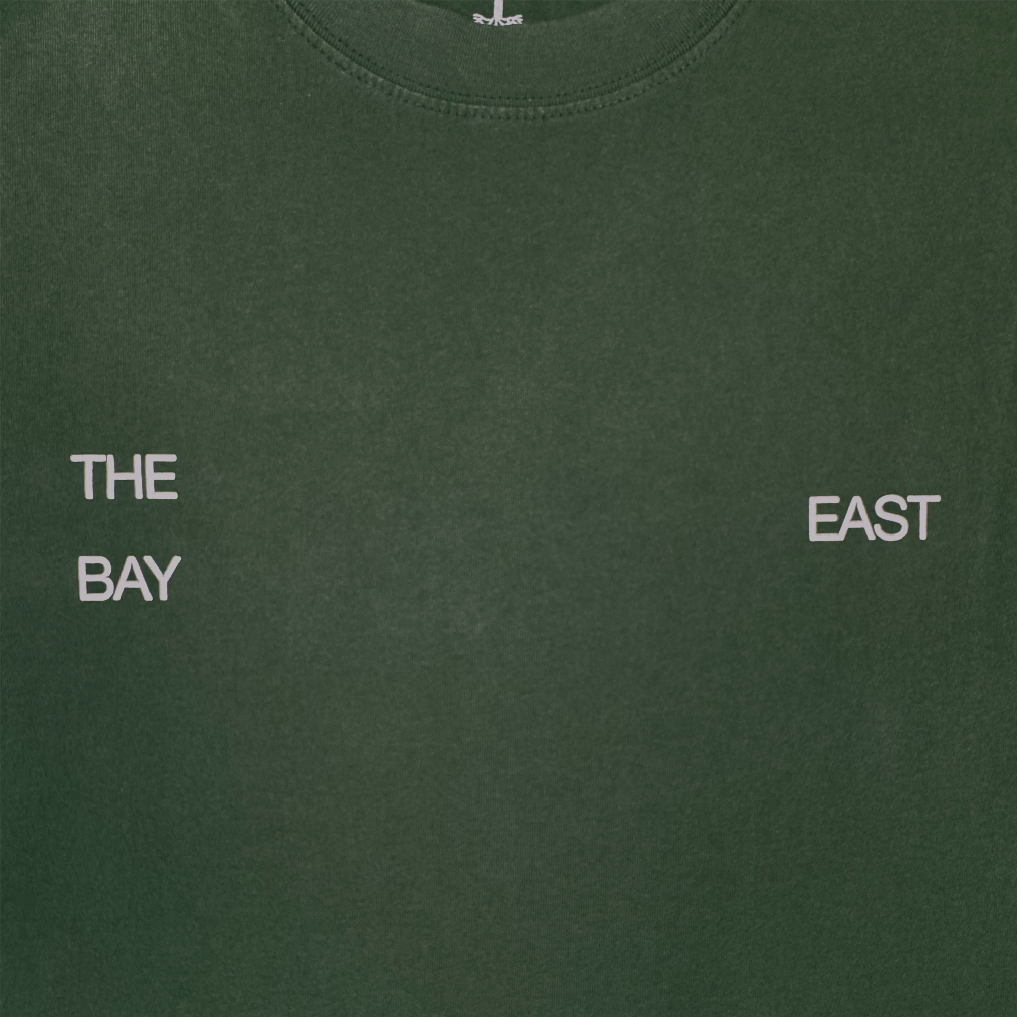 The East Bay Tee by Oaklandish is a dark green t-shirt featuring white, spaced-out text: "THE" above "BAY" on the left chest and "EAST" on the right chest. This design subtly nods to a Toro y Moi collaboration and Chaz Bear’s classic t-shirt style.