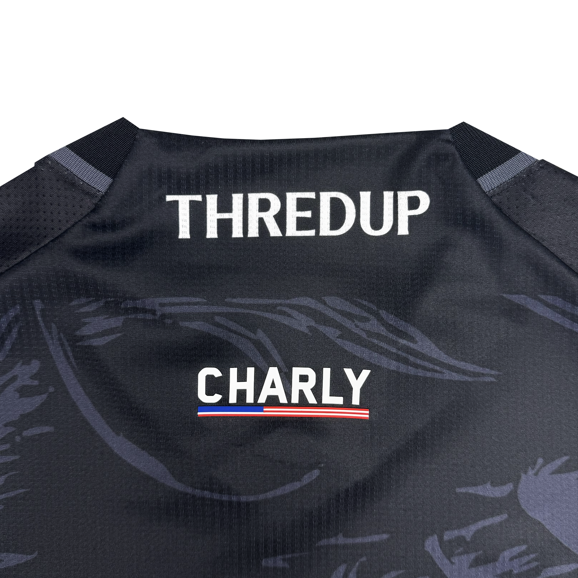 Close-up of the Unisex Oak-ness Awakens Kit by Oakland Roots SC—a black jersey with “THREDUP” in bold white, “CHARLY” below, and a red, white, and blue stripe—featuring subtle patterns inspired by the legendary Oak-ness Monster.