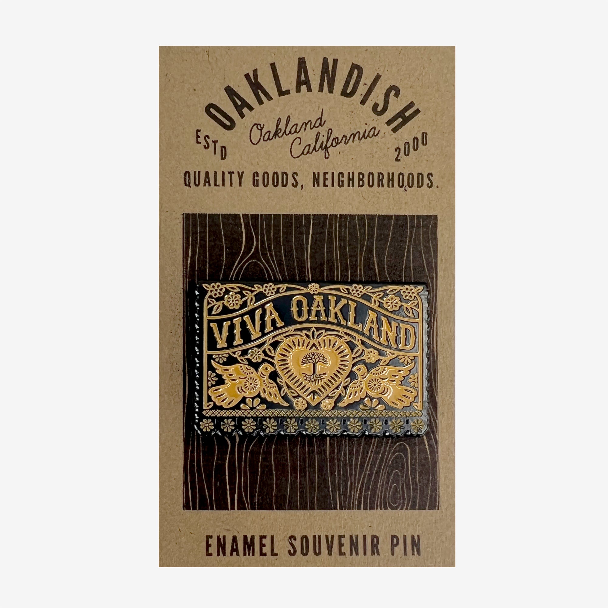 Gold and black enamel pin Viva Oakland wordmark with heart, birds and flowers on brown paper retail packaging.