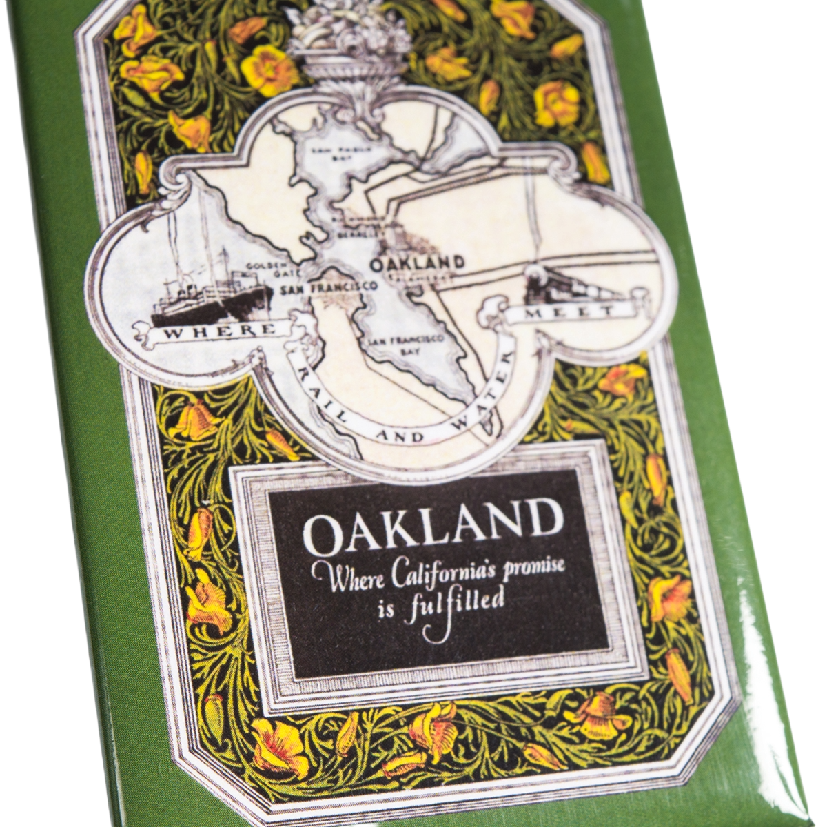 A green Rail and Sea Magnet by Oaklandish showcases a vintage map of Oakland and San Francisco above elegant floral decorations. A black box with white text underneath reads: “OAKLAND Where California’s promise is fulfilled.” Ornate yellow flowers frame the map and message, making this eye-catching magnet an ideal Oakland souvenir or a unique California-inspired accessory.