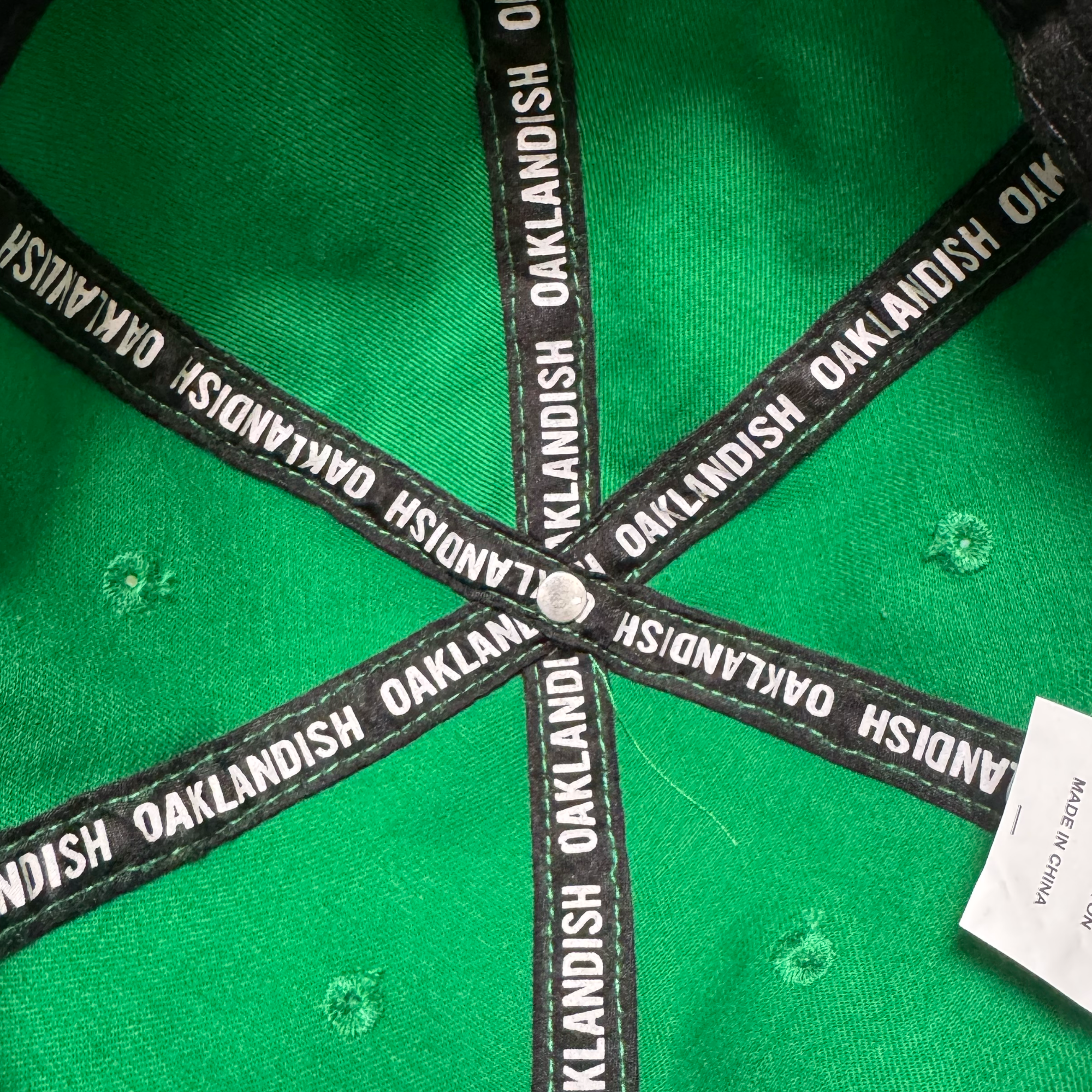 Inside the Oakland Ballers Dad Hat by Oakland Ballers: green with black trim, “OAKLANDISH” in white along the seams, a central metal button, and a partially visible white tag on the right. Inspired by Oakland's baseball spirit.