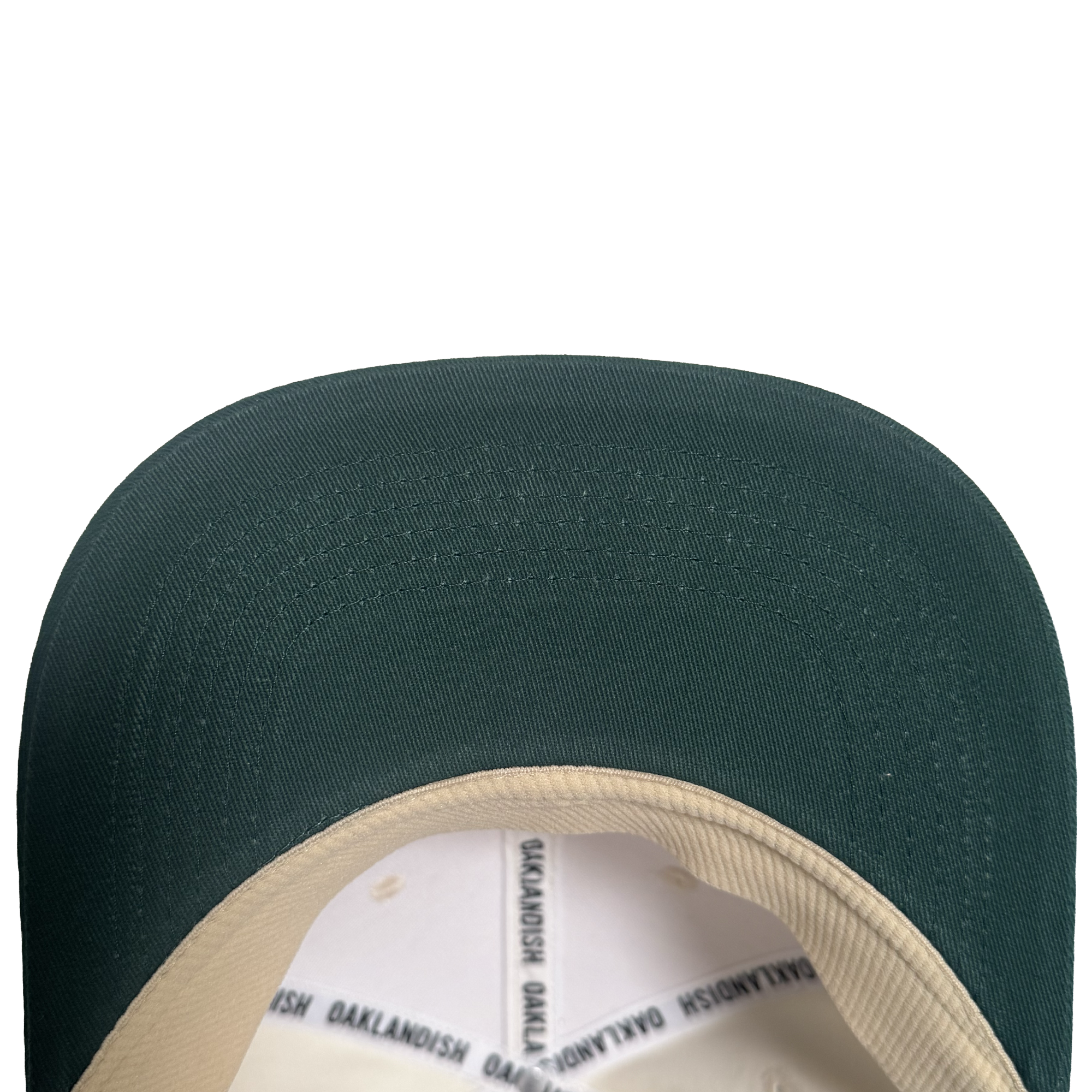 Close-up view of the brim and part of the inner lining of the Oakland Peloteros Hat by Oakland Ballers. The hat features a green brim and a beige inner lining with repeating black "OAKLANDISH" text. Set against a plain white background, only the top portion of this classic design is visible—a stylish nod to Oakland baseball team pride.