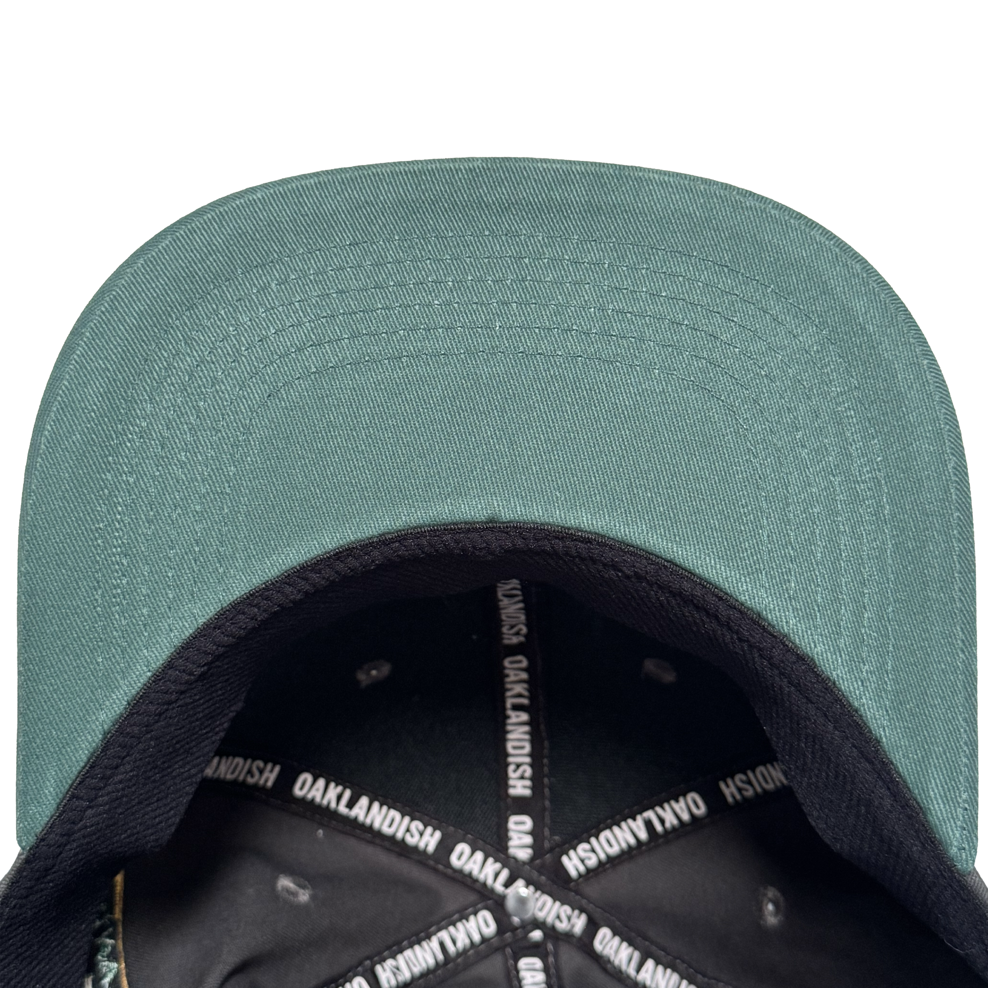 A top-down view of the Oakland Ballers Logo Hat by Oakland Ballers shows the green cap with black brim, white “OAKLANDISH” text on the inner band, and metal rivets around the crown, celebrating the Oakland baseball team.
