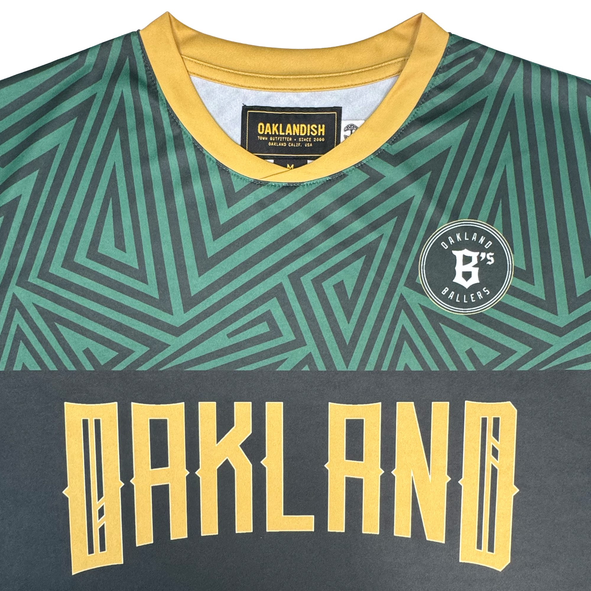 A close-up of the Oakland Ballers SC Jersey, a pro baseball jersey featuring green geometric patterns, a yellow collar, bold yellow "OAKLAND" lettering on the front, and a round patch reading "Oakland B's Ballers." The brand label inside the collar displays "Oakland Ballers," capturing the spirit of the Oakland Ballers baseball team.