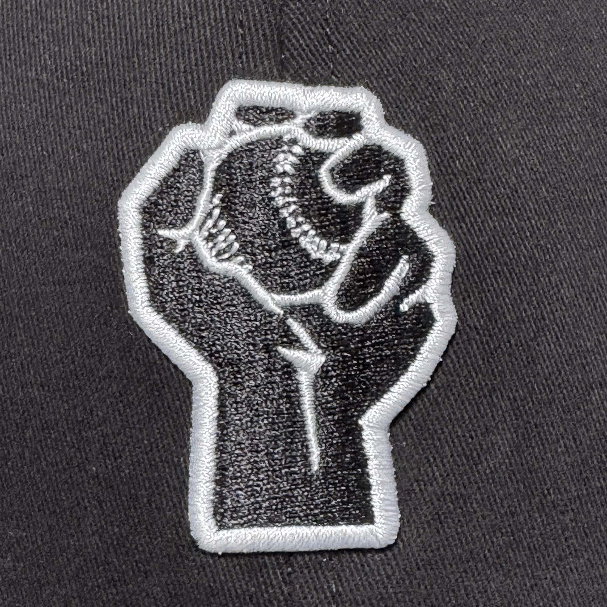 The Oakland Stand Up Hat by Oakland Ballers features a black and white embroidered patch of a raised fist holding a baseball, symbolizing solidarity and the spirit of the city’s newest Pioneer League team.