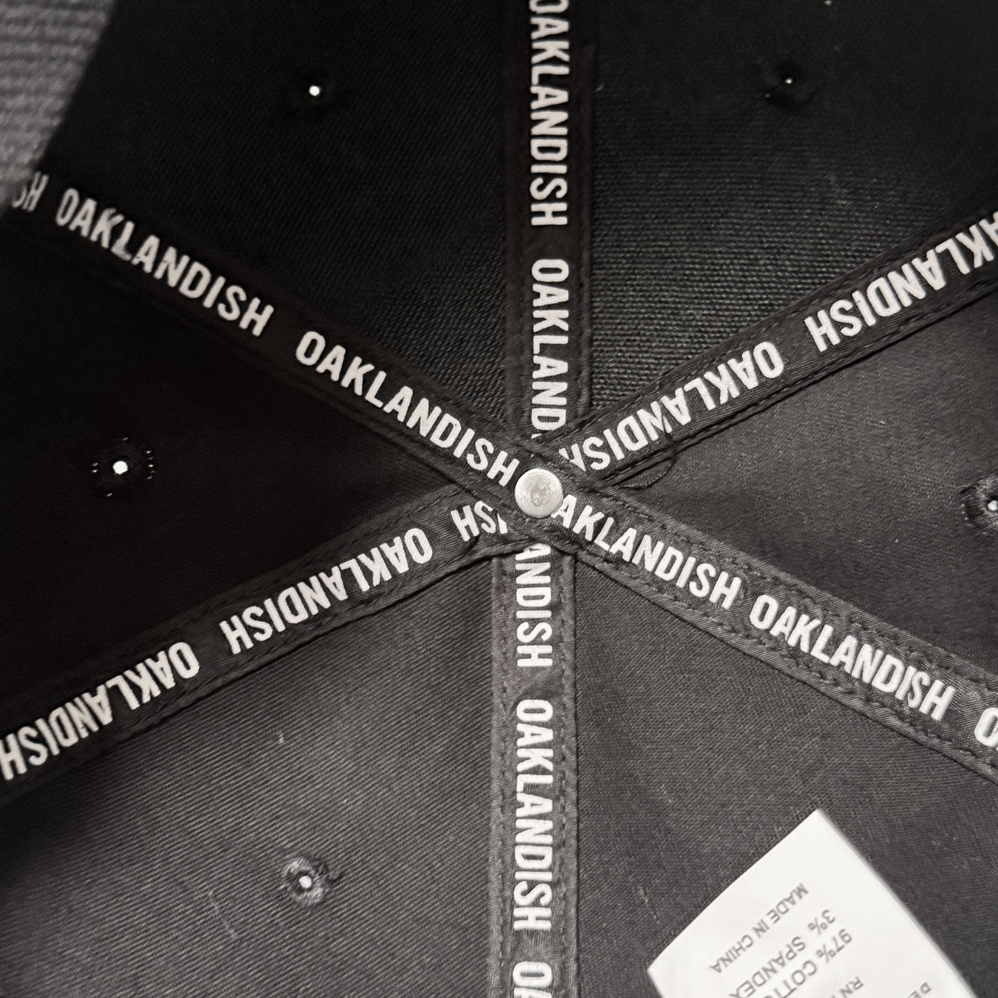 Interior view of the Oakland Stand Up Hat by Oakland Ballers, featuring crisscrossed black bands with “OAKLANDISH” in white, a metallic button, small eyelets, and a white fabric tag—celebrating the Pioneer League team.