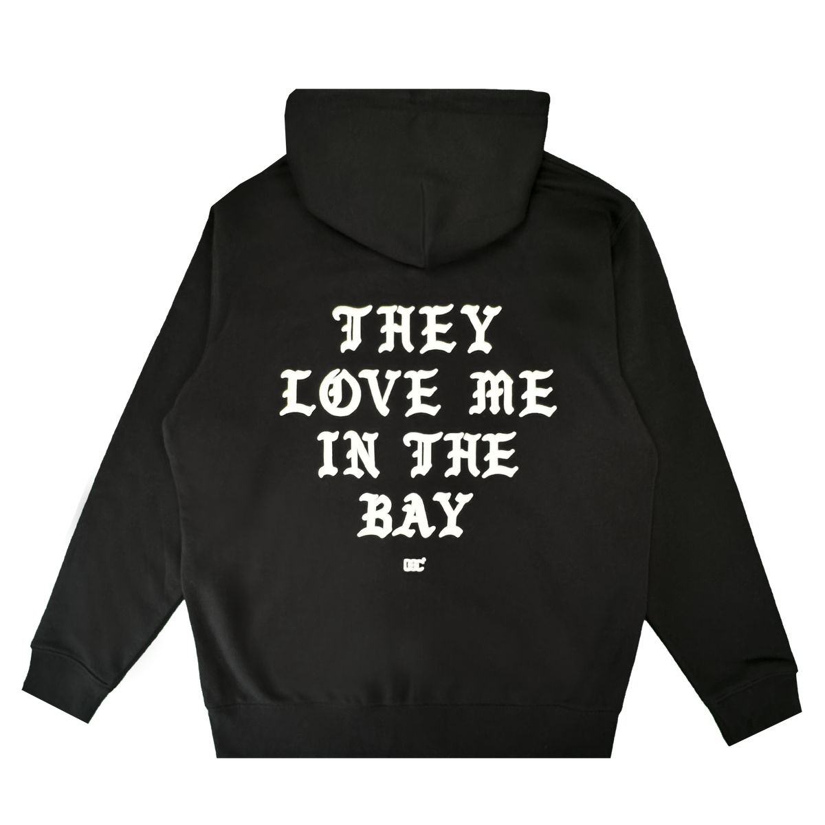 A black heavyweight fleece zip hoodie from By DOC’s They Love Me Zip collection, featuring white gothic-style text on the back that reads “THEY LOVE ME IN THE BAY” with a small white logo beneath it, laid flat on a white background.