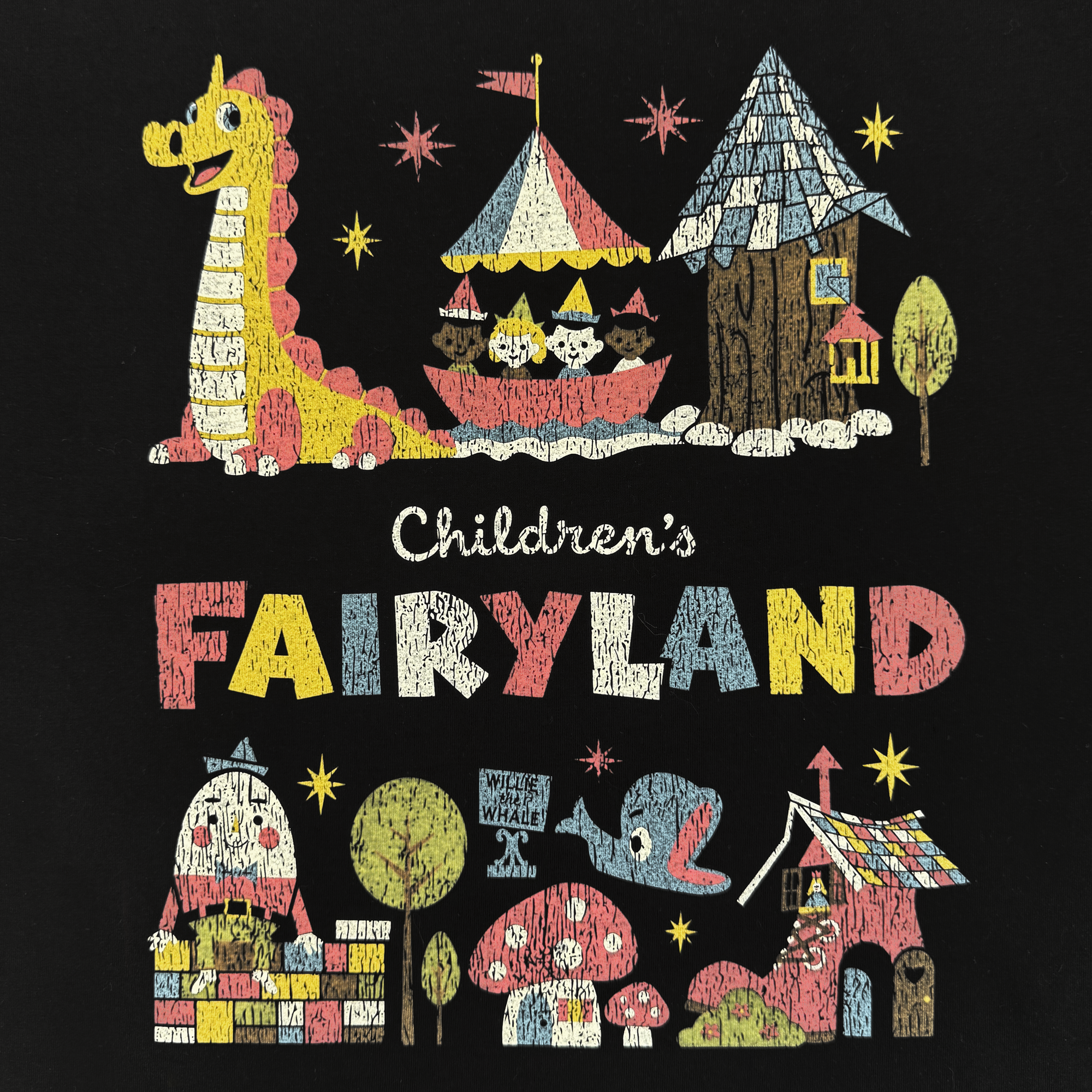 The Oaklandish Starlit Tee features a vibrant, textured illustration on black with Fairyland icons: dragon, circus tent, cottage, tree, “Children’s FAIRYLAND” lettering, whimsical houses, smiling whale, and red mushroom.