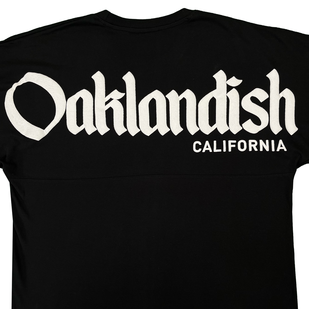 A black Oaklandish Temple LS Tee for men, made from 100% cotton, features large white Old English “Oaklandish” lettering across the upper back with “California” printed in smaller plain white text below and to the right. The shirt is displayed against a clean white background.