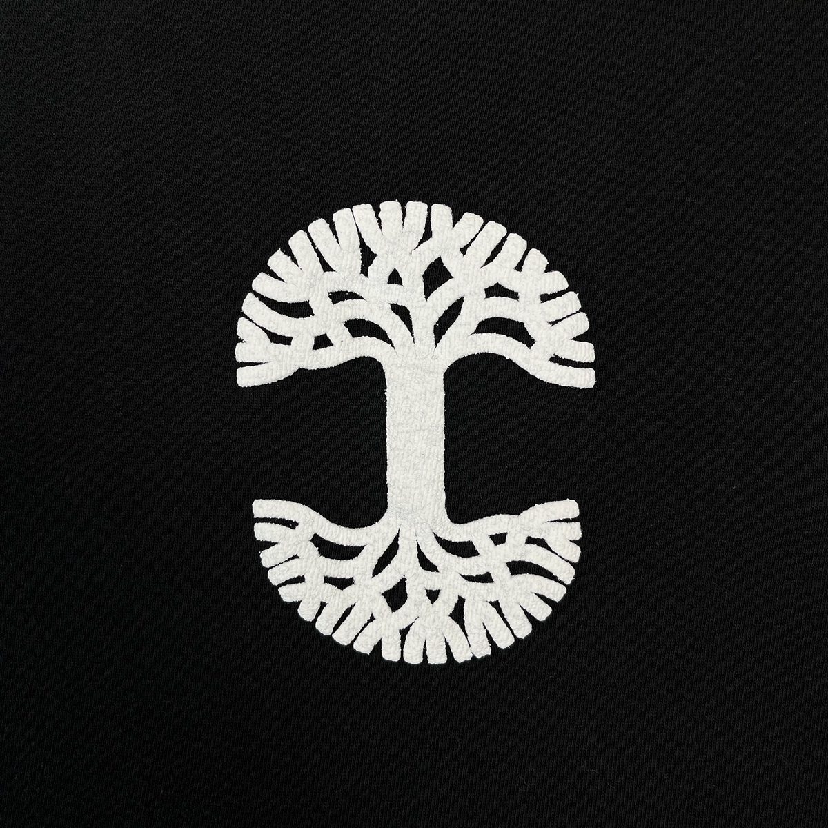 The Oaklandish Temple LS Tee features a striking white tree design with mirrored branches and roots, creating a symmetrical circular pattern reminiscent of both a tree and the letter “C” on a black background. Printed on 100% cotton, this men’s heavy-weight long sleeve t-shirt combines comfort with lasting durability.