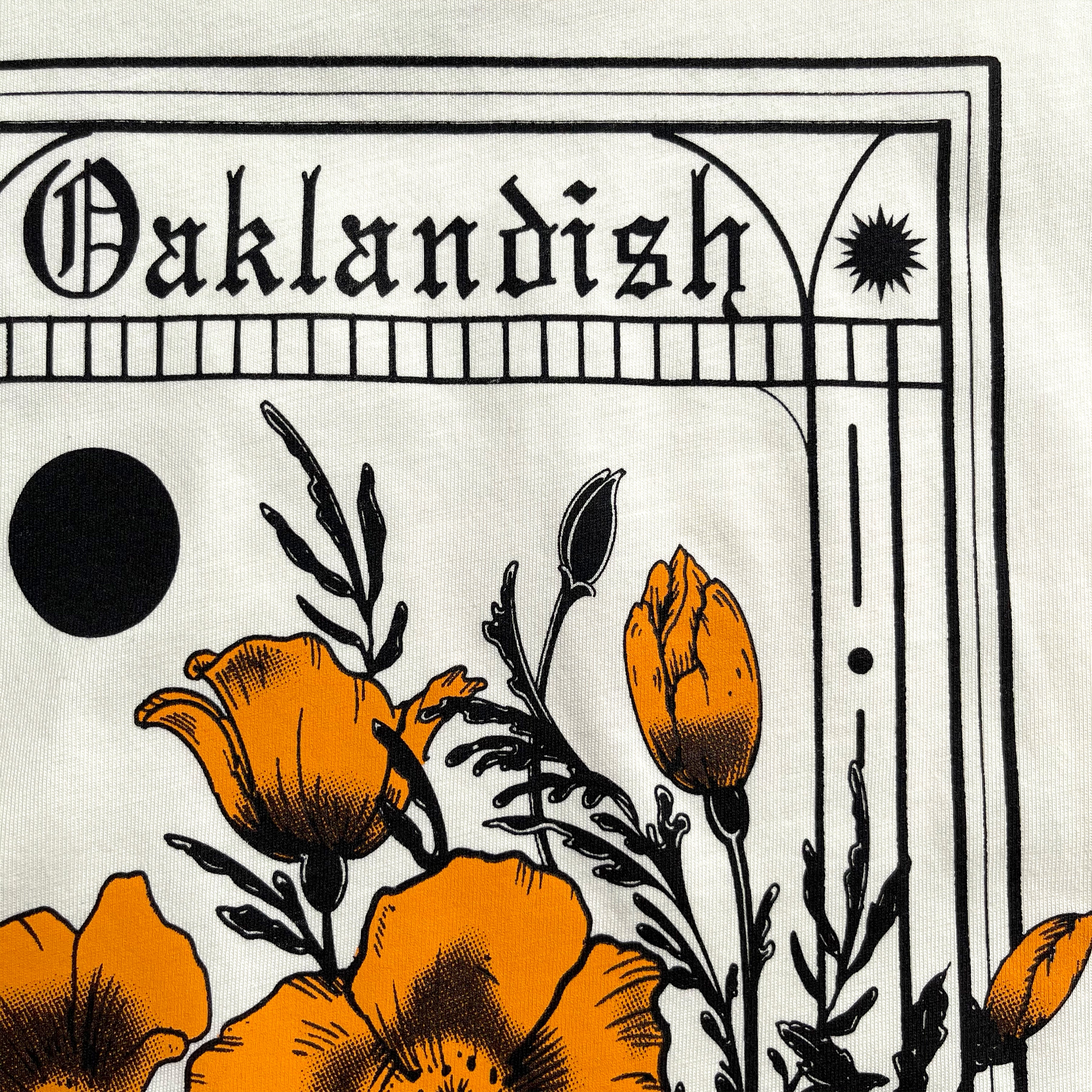 The Blossom Tee by Oaklandish showcases a close-up of a design with the word "Oaklandish" in gothic script at the top. Below, orange poppies with black outlines and stems are depicted against a light-colored background, complemented by additional decorative elements like a black circle and a star. This classic fit t-shirt is made of 100% cotton.